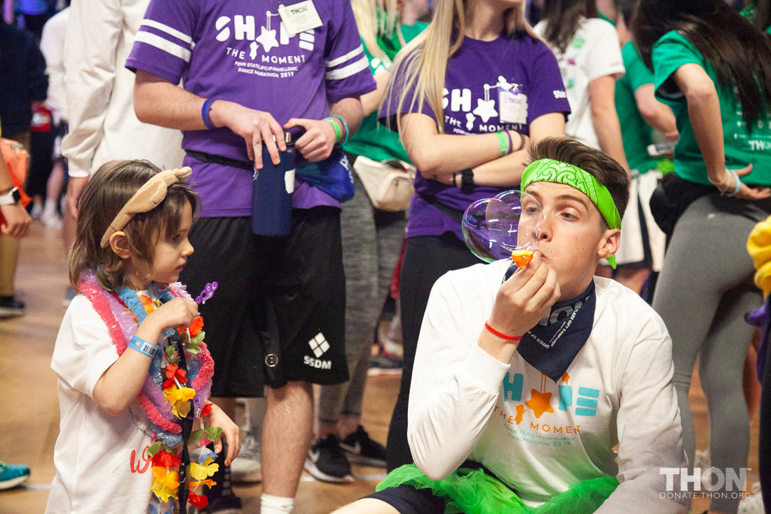 Image: A child watches a college student blow bubbles as others look on